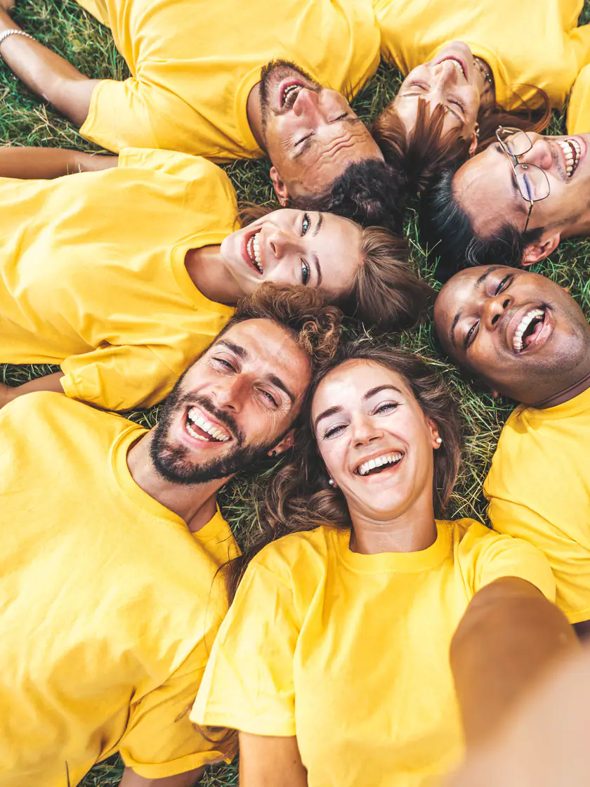 Grupo de amigos de camiseta amarela deitados em roda na grama, rindo