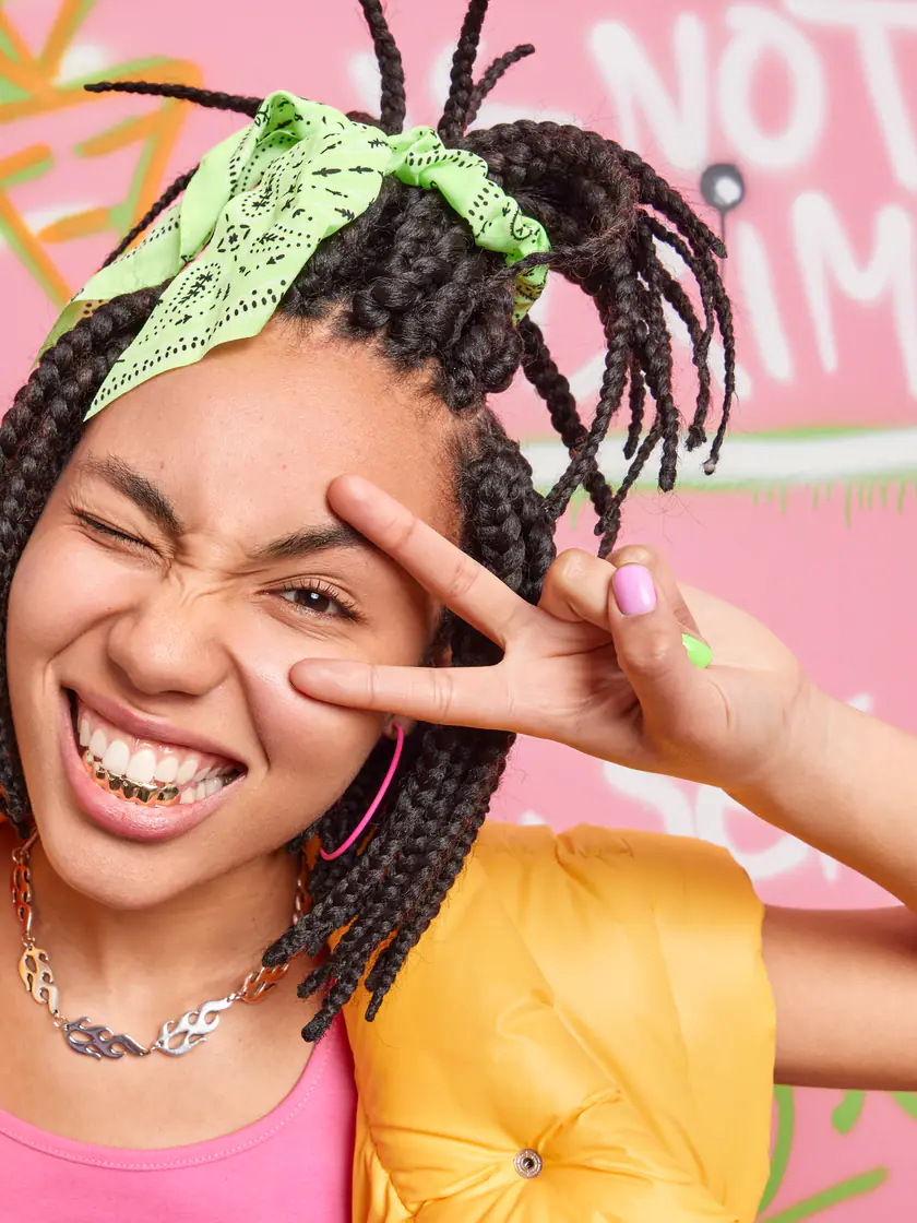 Artista de tranças sorrindo em frente a um muro grafitado