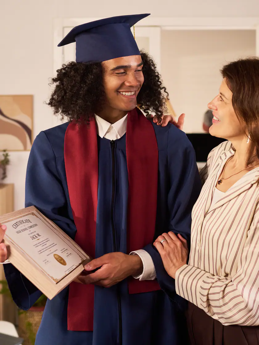 Jovem de beca segurando o diploma ao lado da mãe