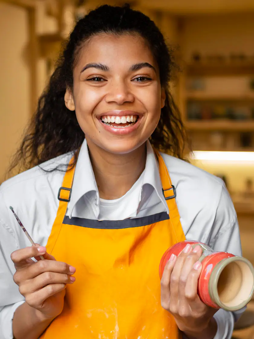 Ceramista de avental amarelo sorrindo no próprio ateliê