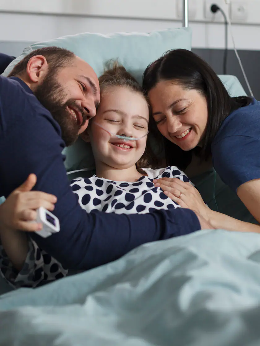 Pai e mãe abraçando a filha sorridente em um leito de hospital