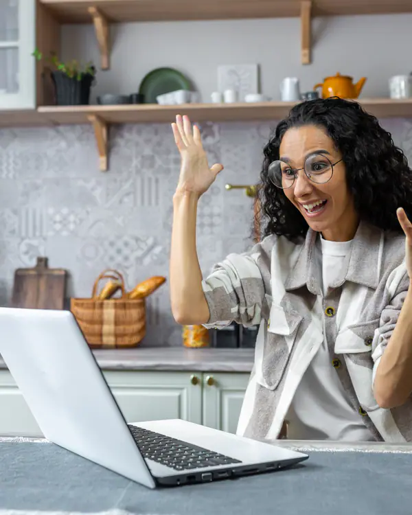 Mulher comemorando em frente ao notebook na cozinha