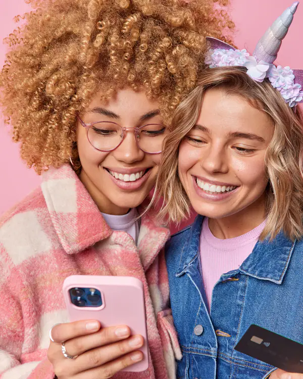 Duas amigas sorrindo com o celular e o cartão na mão